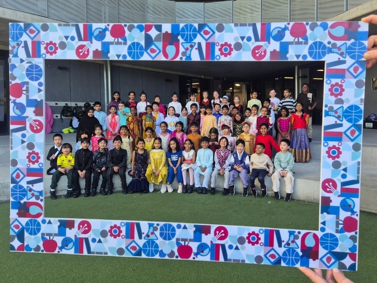 Students in cultural dress posing for a group photo inside a decorative frame.