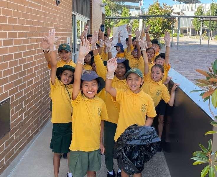 Group of students smiling and raising their hands during an outdoor clean-up activity.