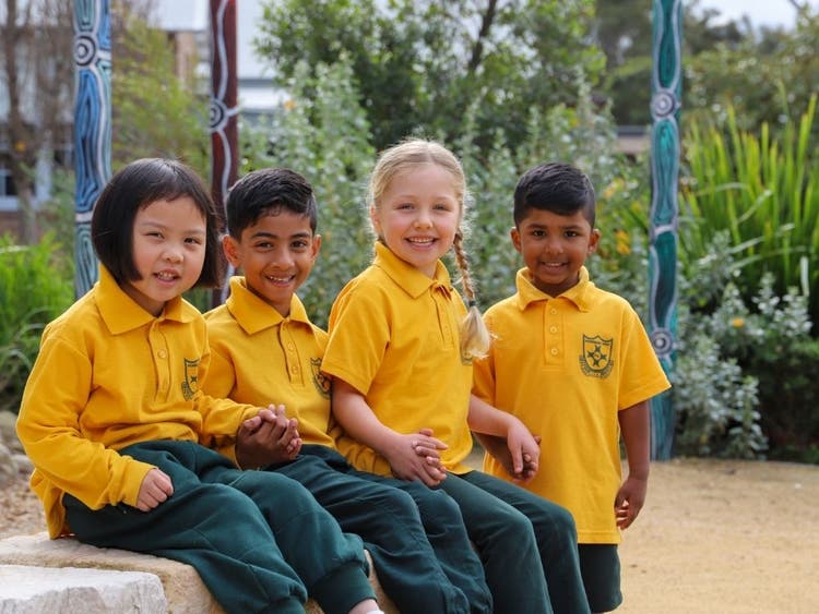 Four students smiling while sitting together in the school garden.