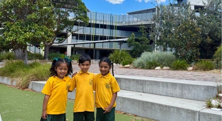 Three students smiling outdoors on the school field.